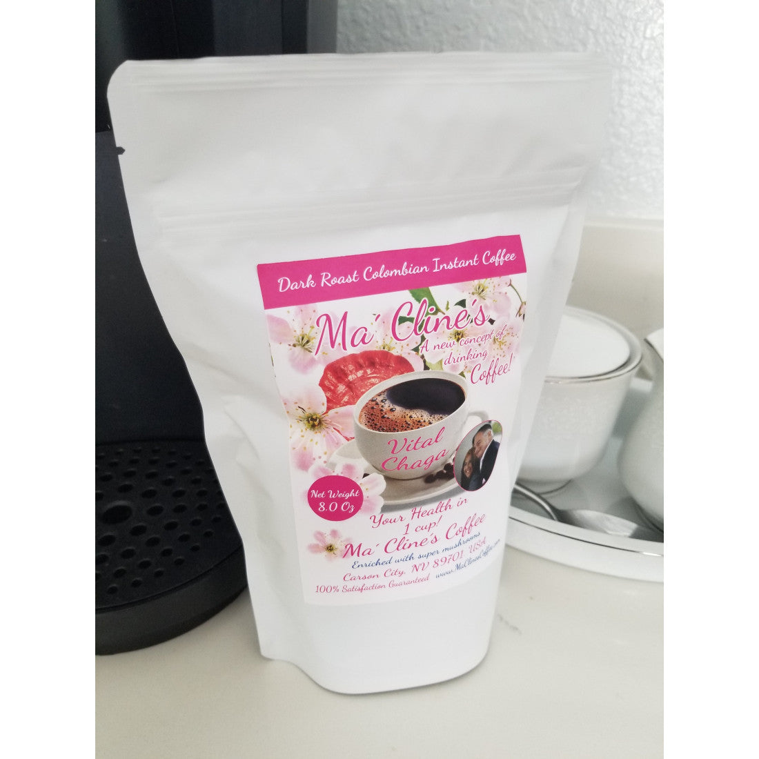 White bag with pink toned front label of Ma' Cline's Vital Instant Coffee. Background photo is pink cherry blossoms, and red ganoderma mushrooms behind a white cup of delicious, steaming coffee.