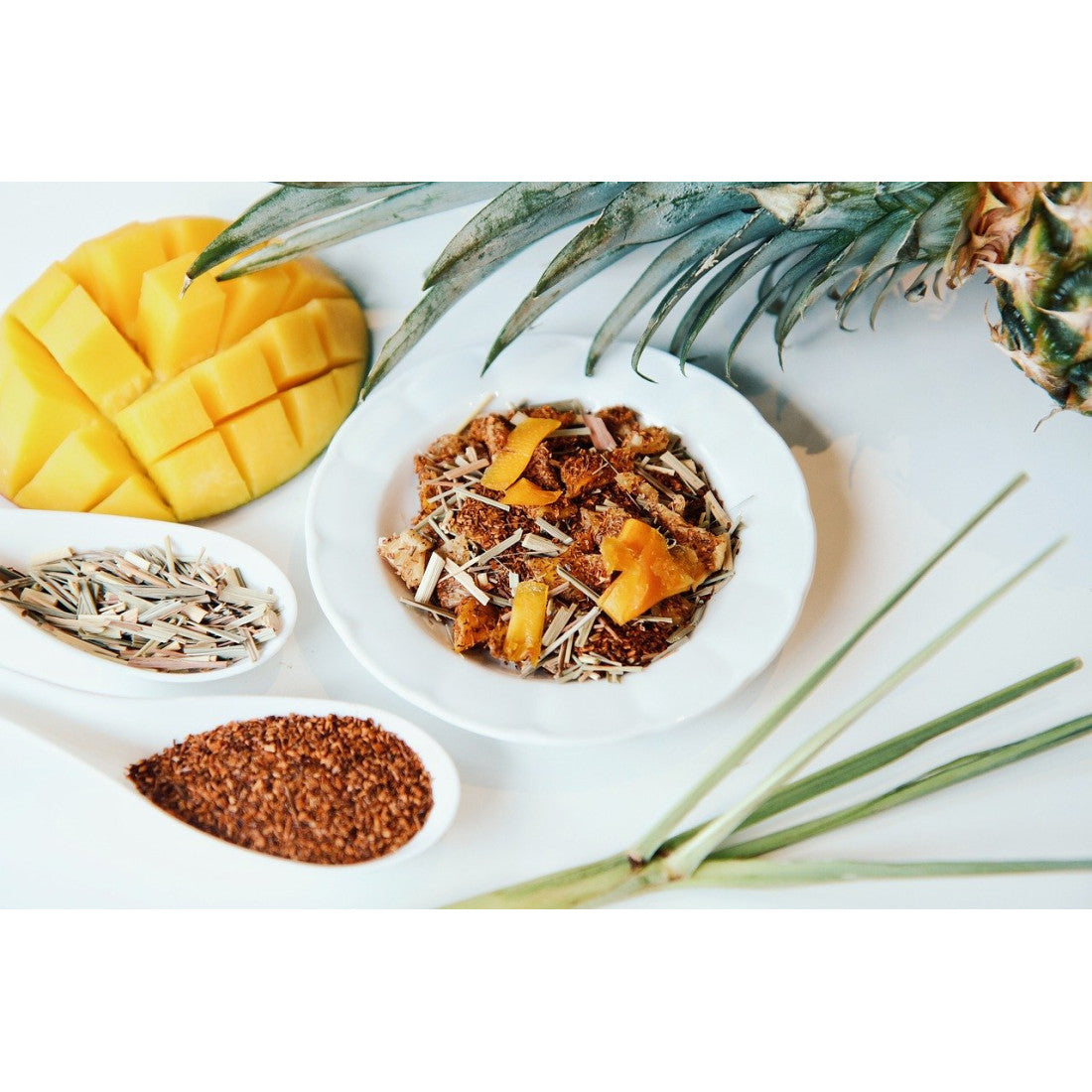 A photo of small plates of ingredients used in our tea blend with the top leves of a pineapple and a decoratively cut mango in the background.
